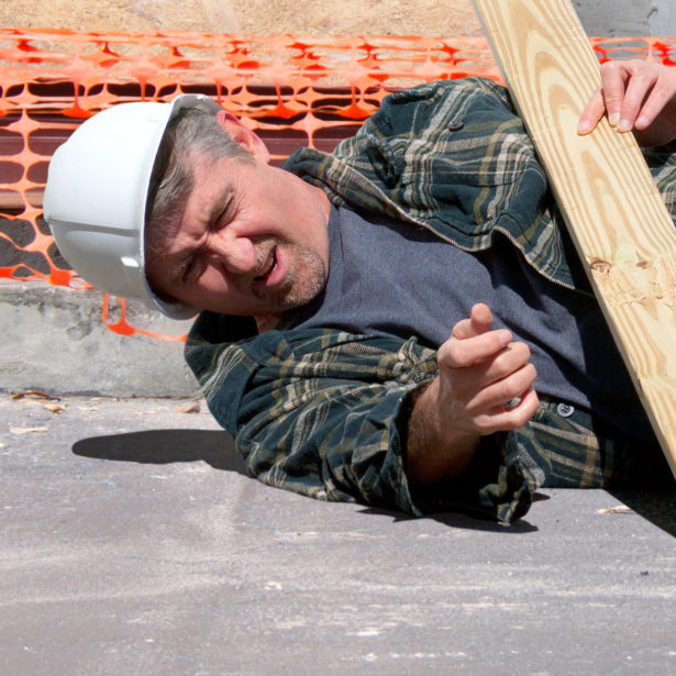 A fallen and injured construction worker in a hard hat laying on the ground at a construction work site
